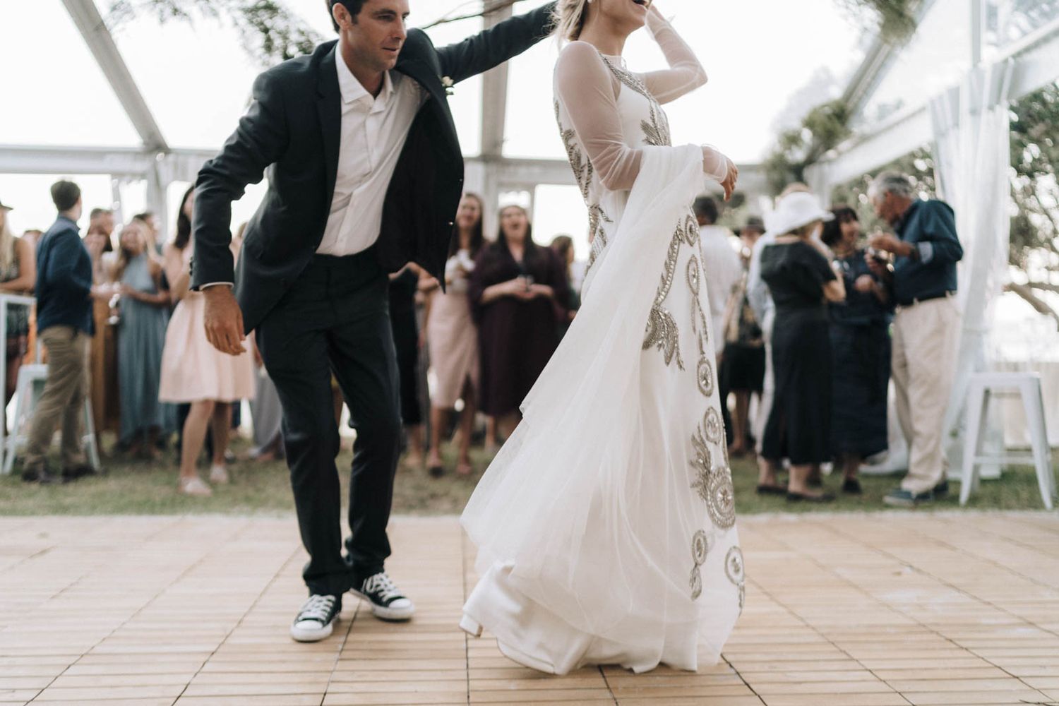 A couple performs their first dance as newlyweds on the dance floor surrounded by guests at their wedding reception.