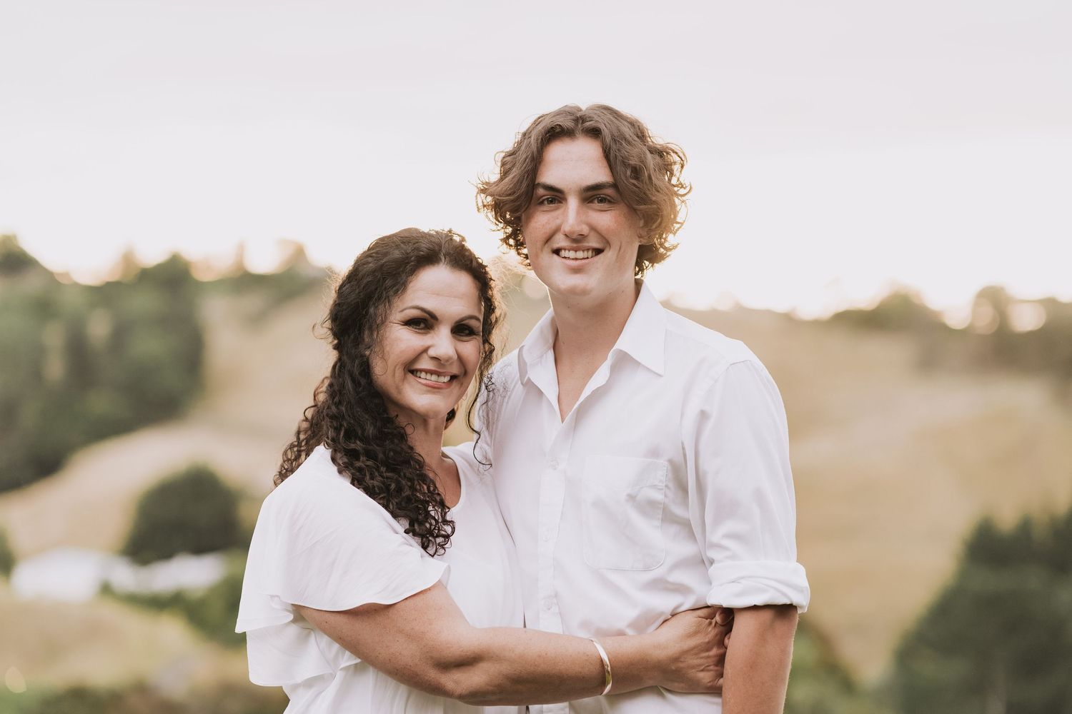 Romantic couple embraces on hillside at sunset creating warm silhouettes against golden light.