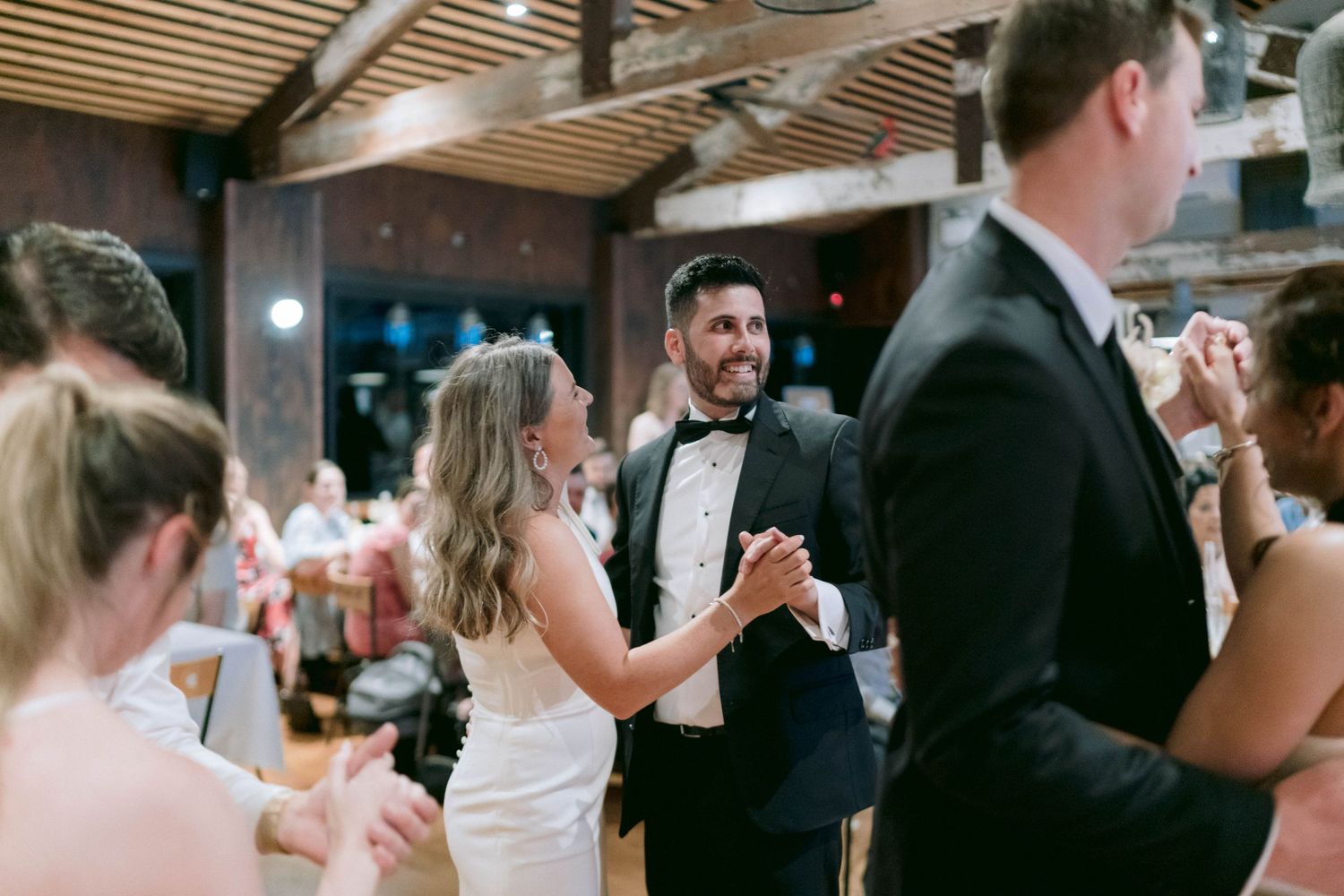 Wedding reception dance floor with guests enjoying celebrations under wooden ceiling beams.