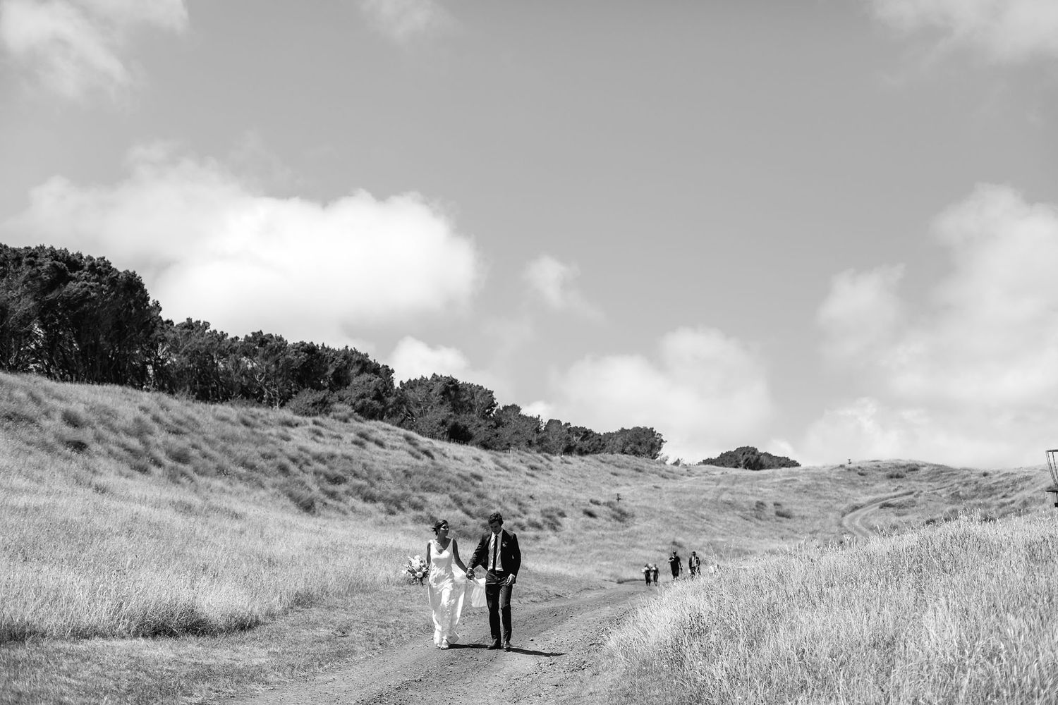 People walking along a winding path through rolling hillsides in black and white captured during an outdoor occasion.