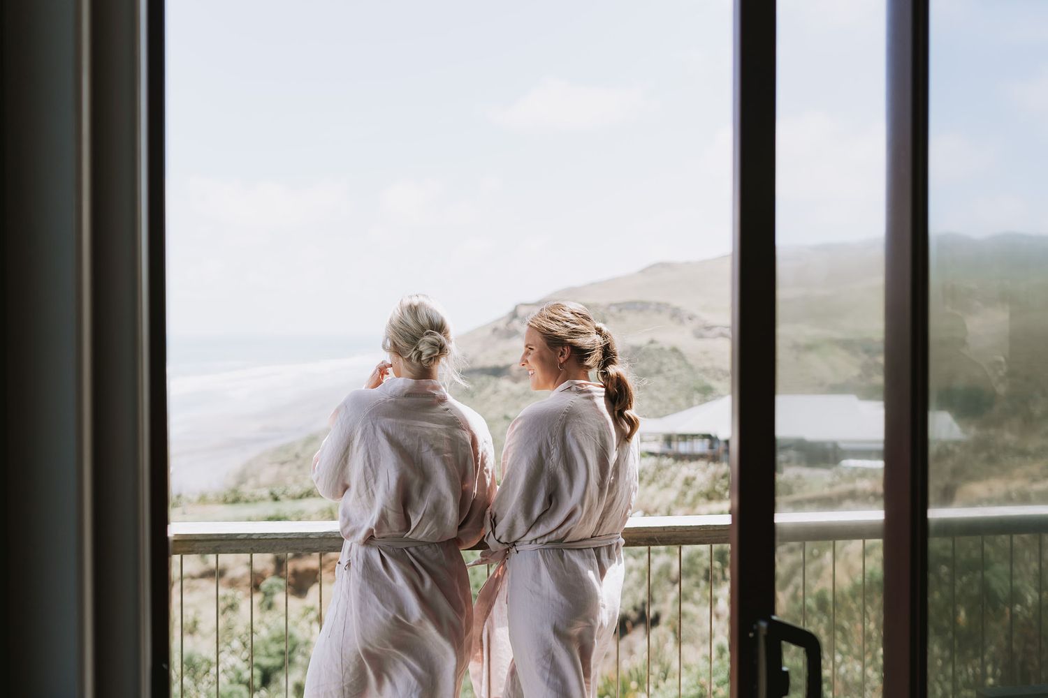 Two people in elegant attire gaze at scenic mountain views through large windows in an indoor space.