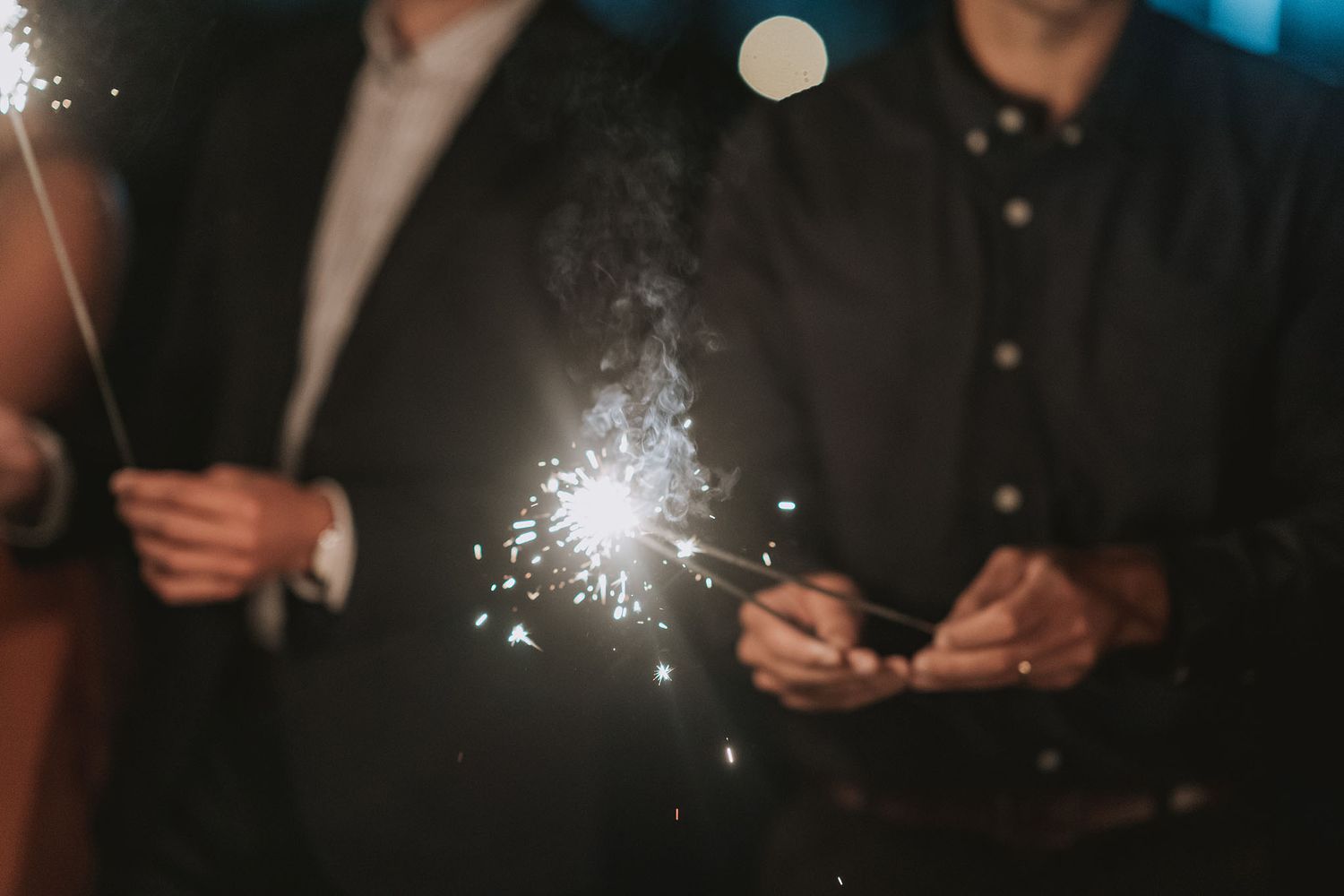 A glowing sparkler creates a bright burst of light against a dark background at a nighttime celebration.