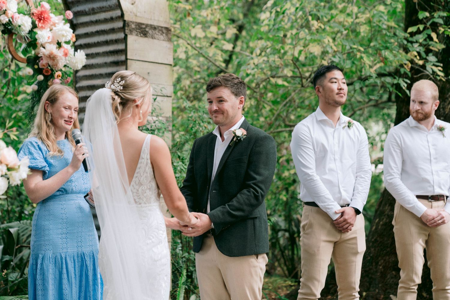 Wedding party lineup with bridesmaids in blue dresses and groomsmen in beige suits outdoors.