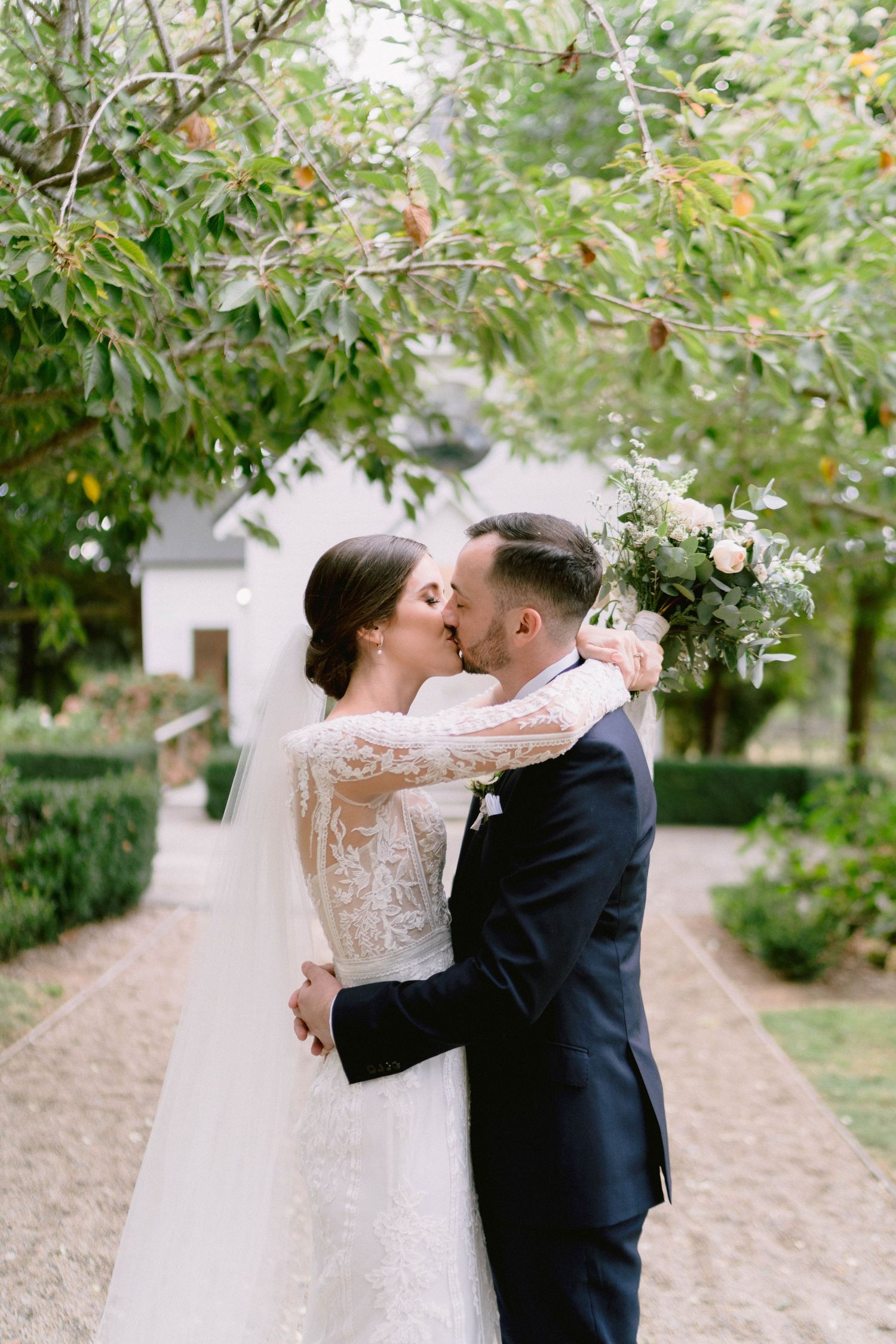 Romantic wedding portrait of couple kissing in a garden pathway.
