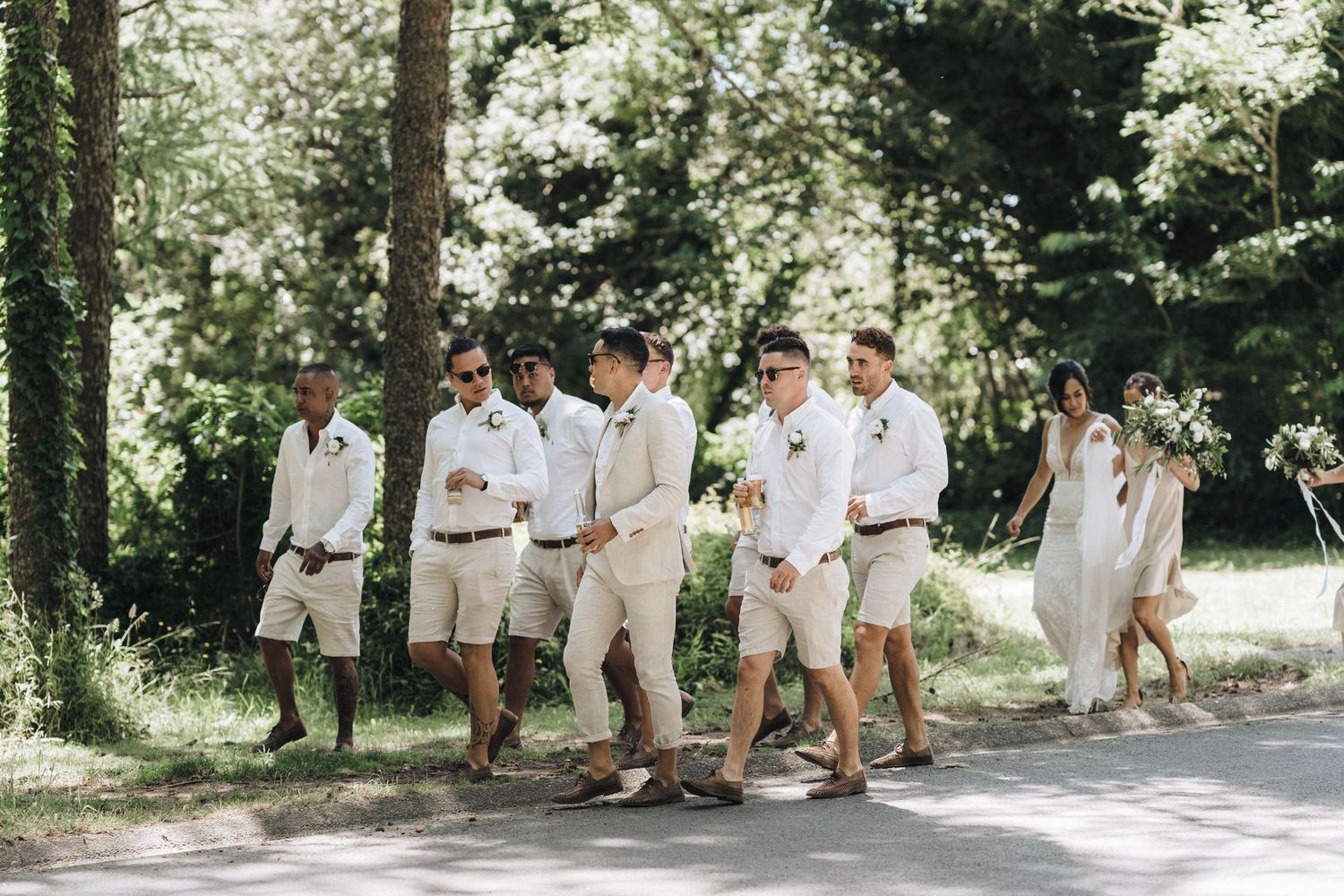 Wedding party groomsmen walking together on sunny path wearing casual khaki and white summer attire.