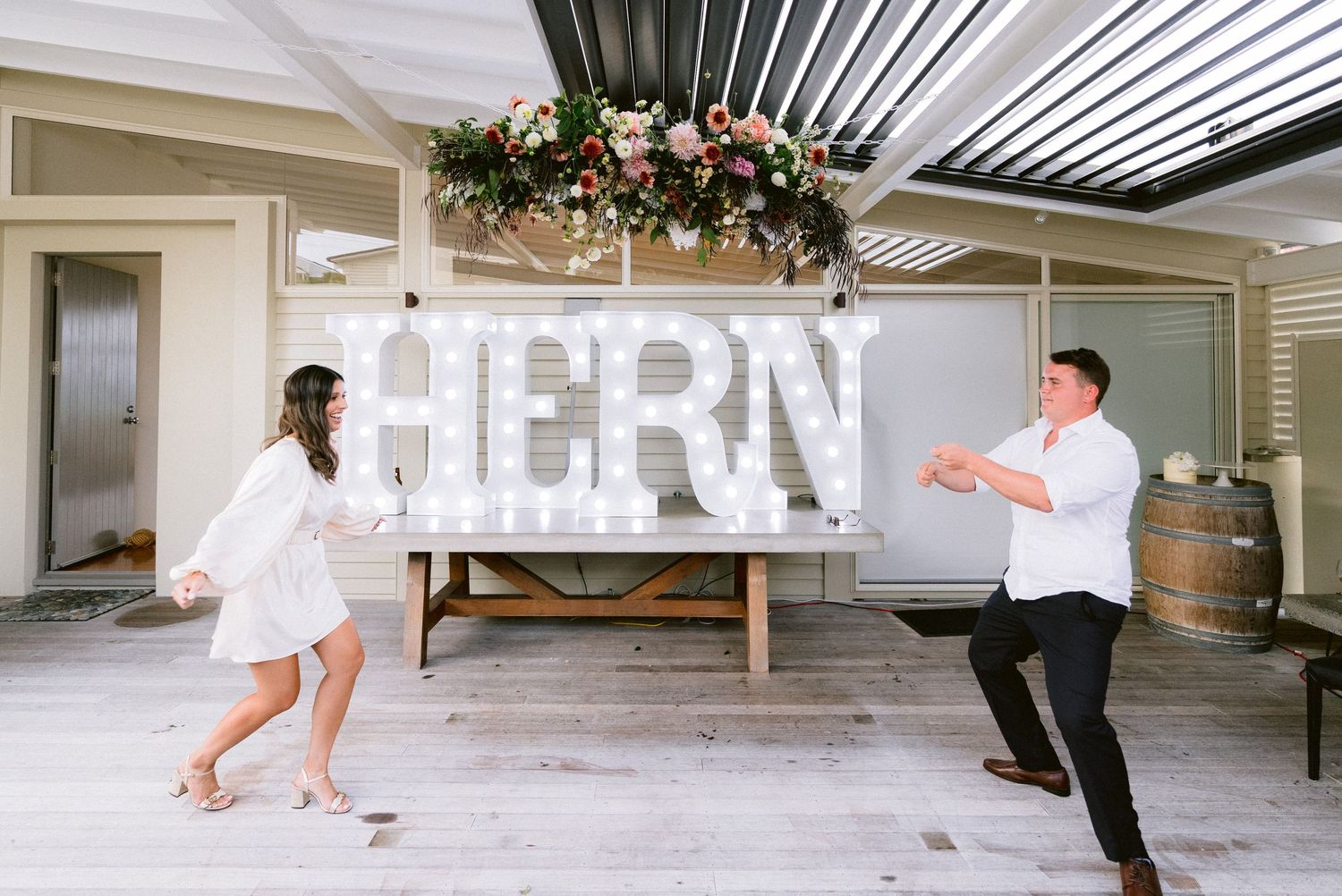 Wedding party members dance and celebrate in a modern white venue space.