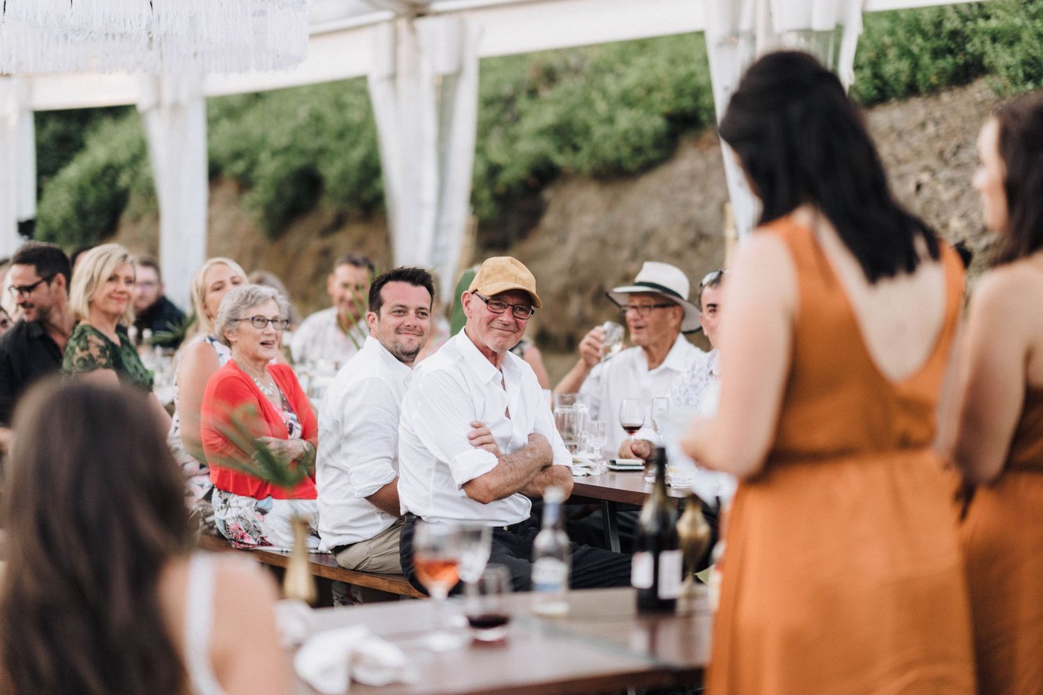 Wedding guests gather under a white canopy for drinks and celebration at an outdoor reception.