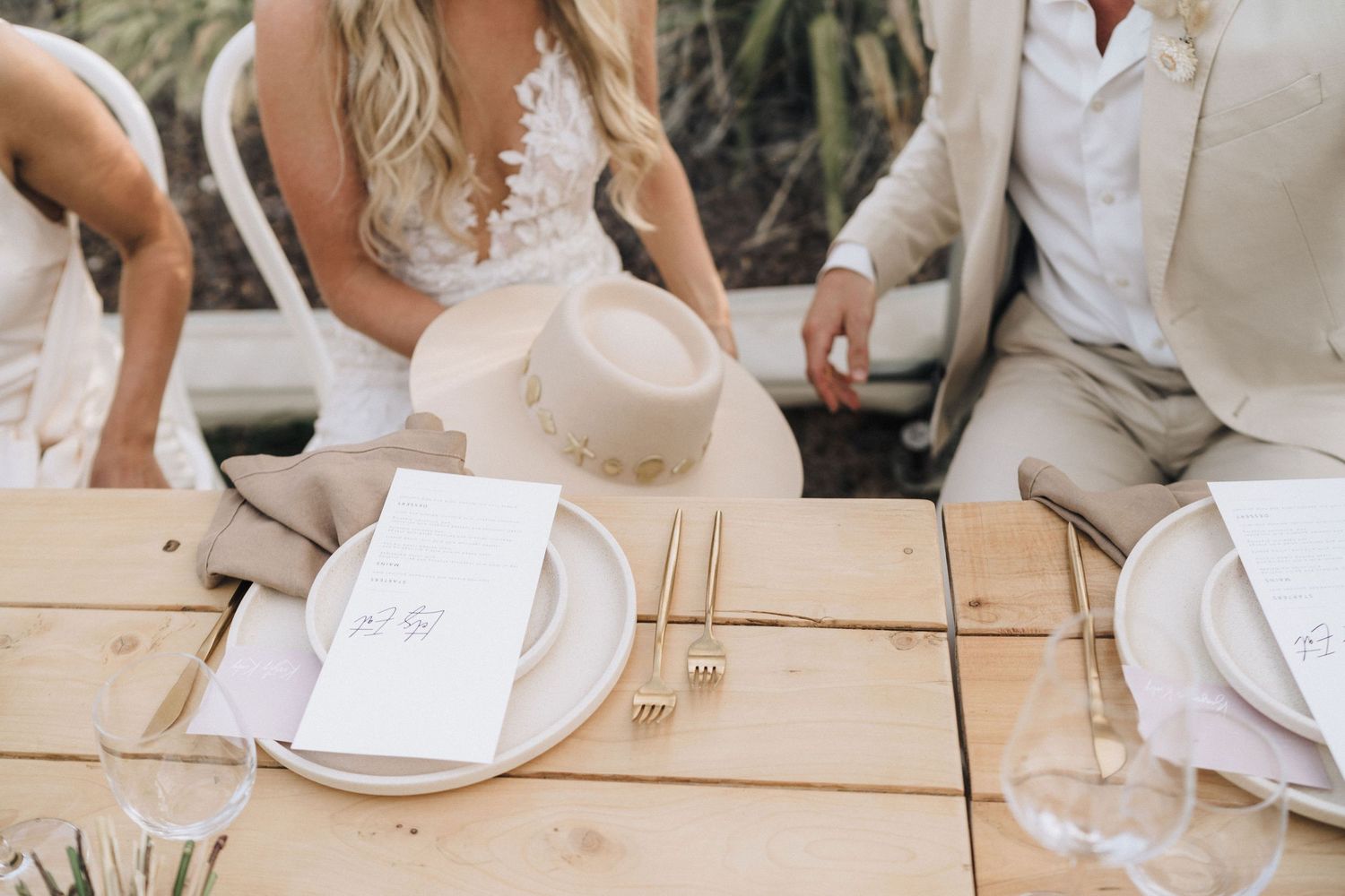 Elegant place settings with white plates and menus on wooden tables at outdoor wedding reception.