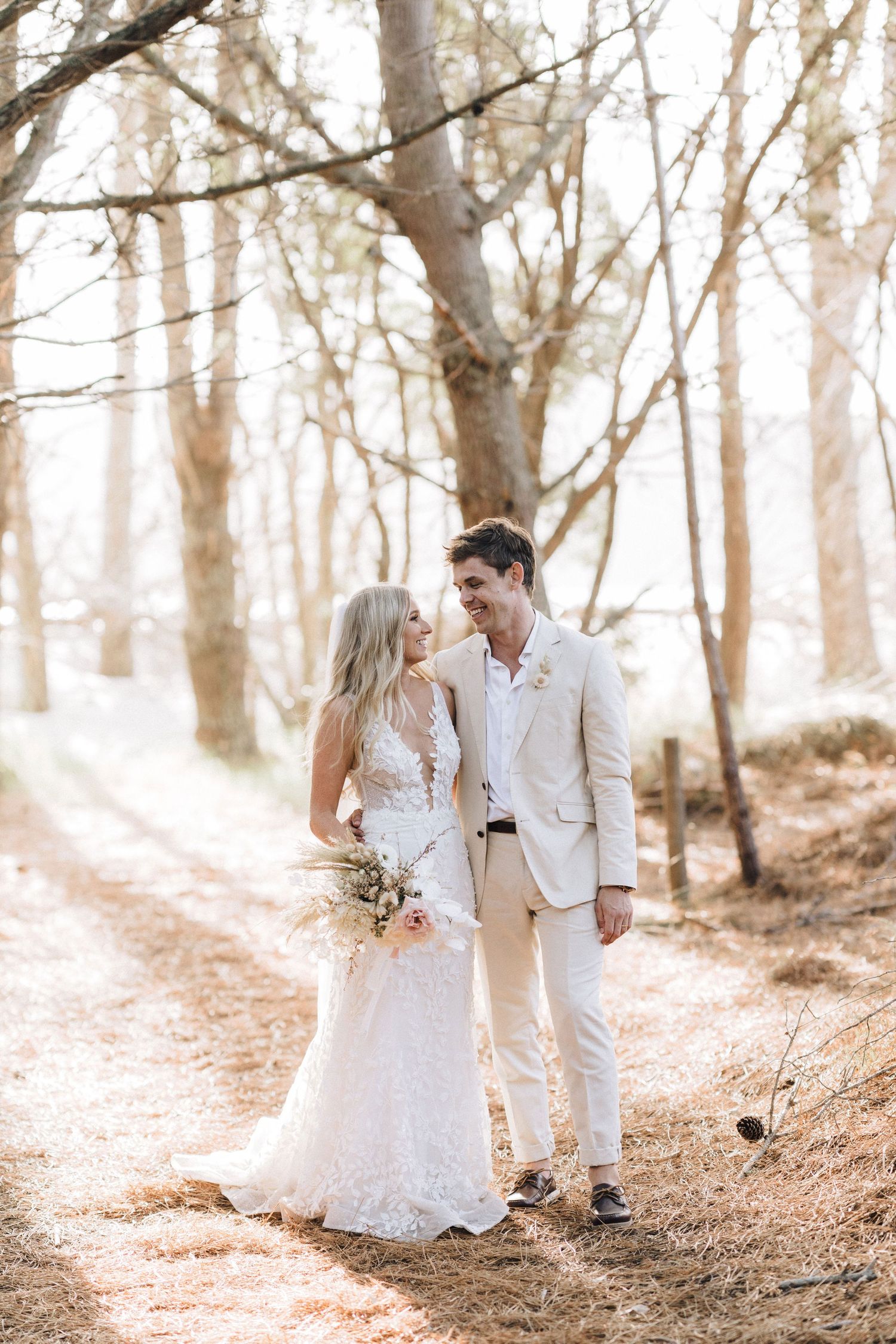 A romantic wedding photo series in a sunlit forest with the couple in white and beige outfits.