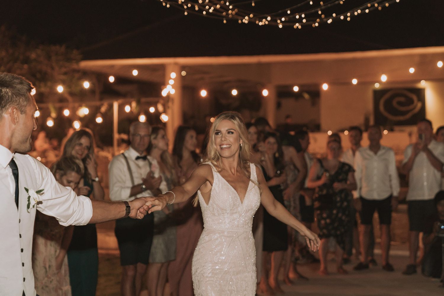 Couple dancing under string lights at outdoor evening reception.