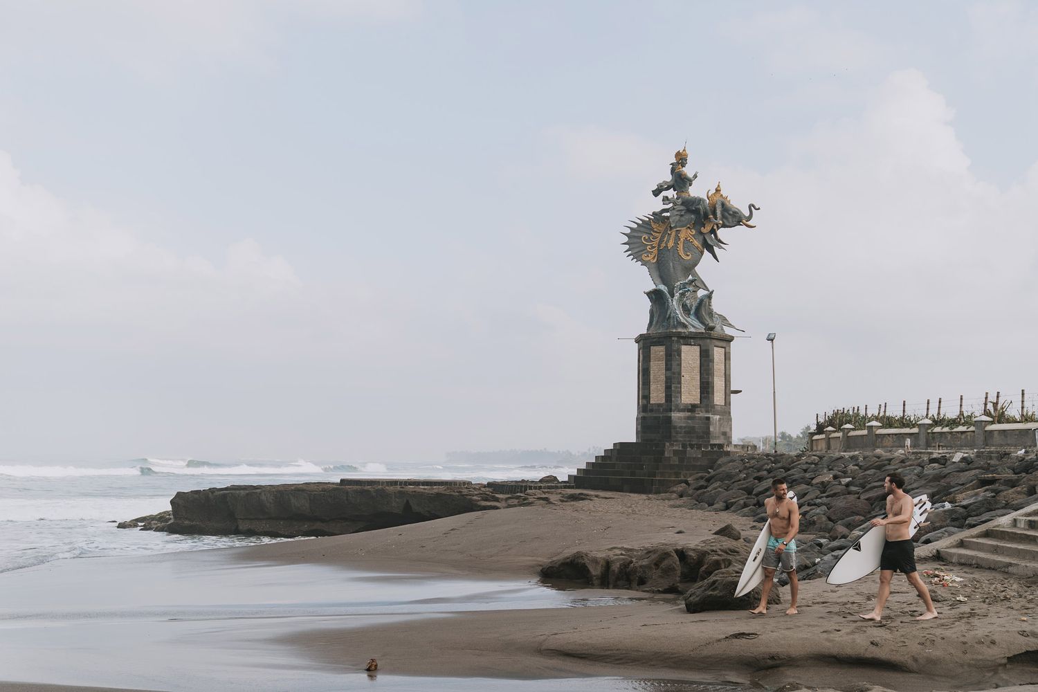 A group of figures explores the rocky coastline with dramatic waves crashing against a lighthouse jetty during stormy weather.