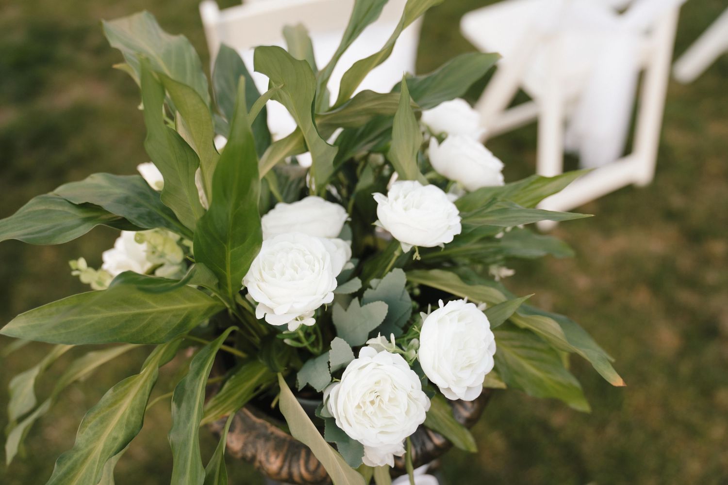 Beautiful white peony flower arrangement with lush green foliage displayed against a natural outdoor background.
