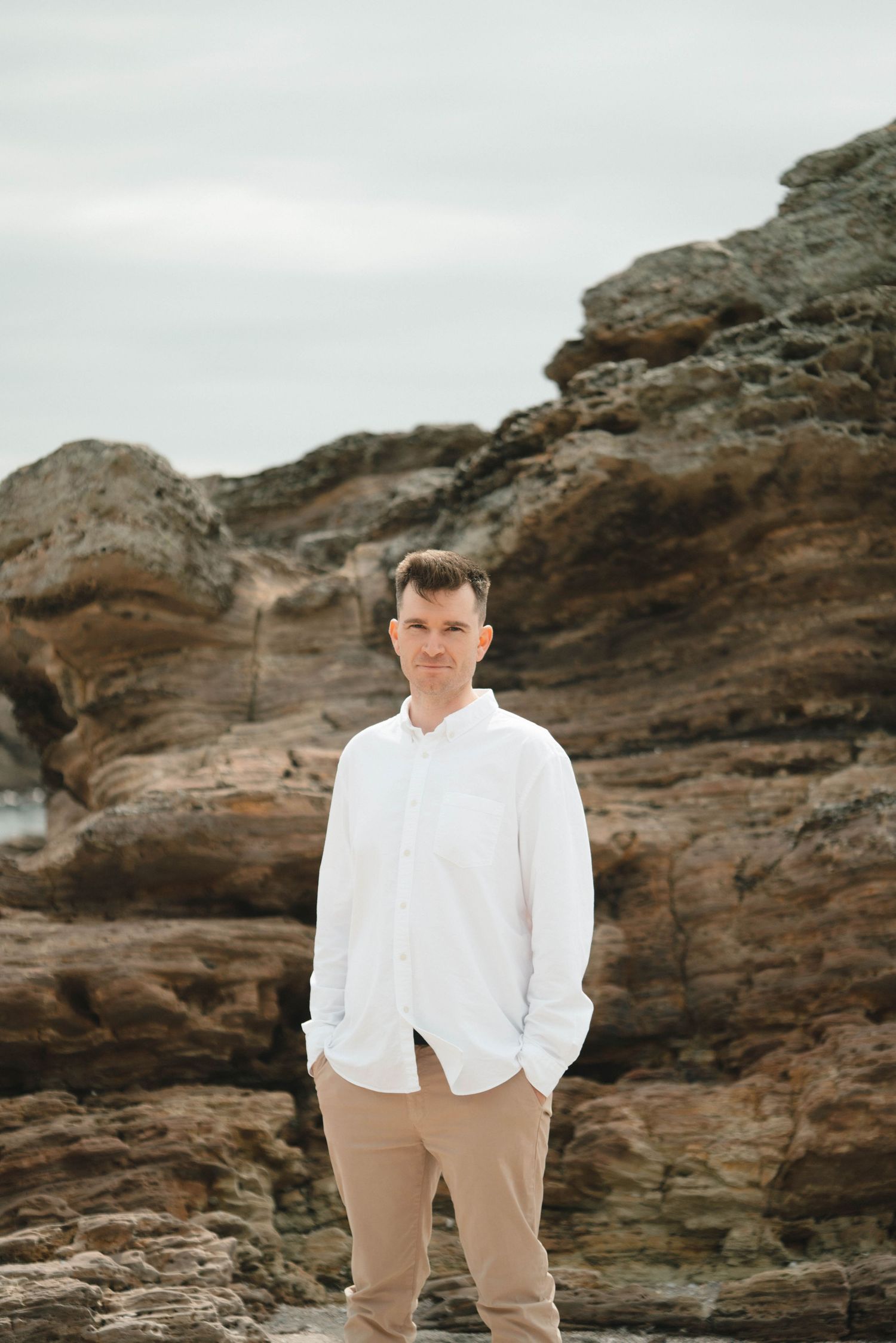 Person in white shirt and khaki pants standing against dramatic coastal rocks.