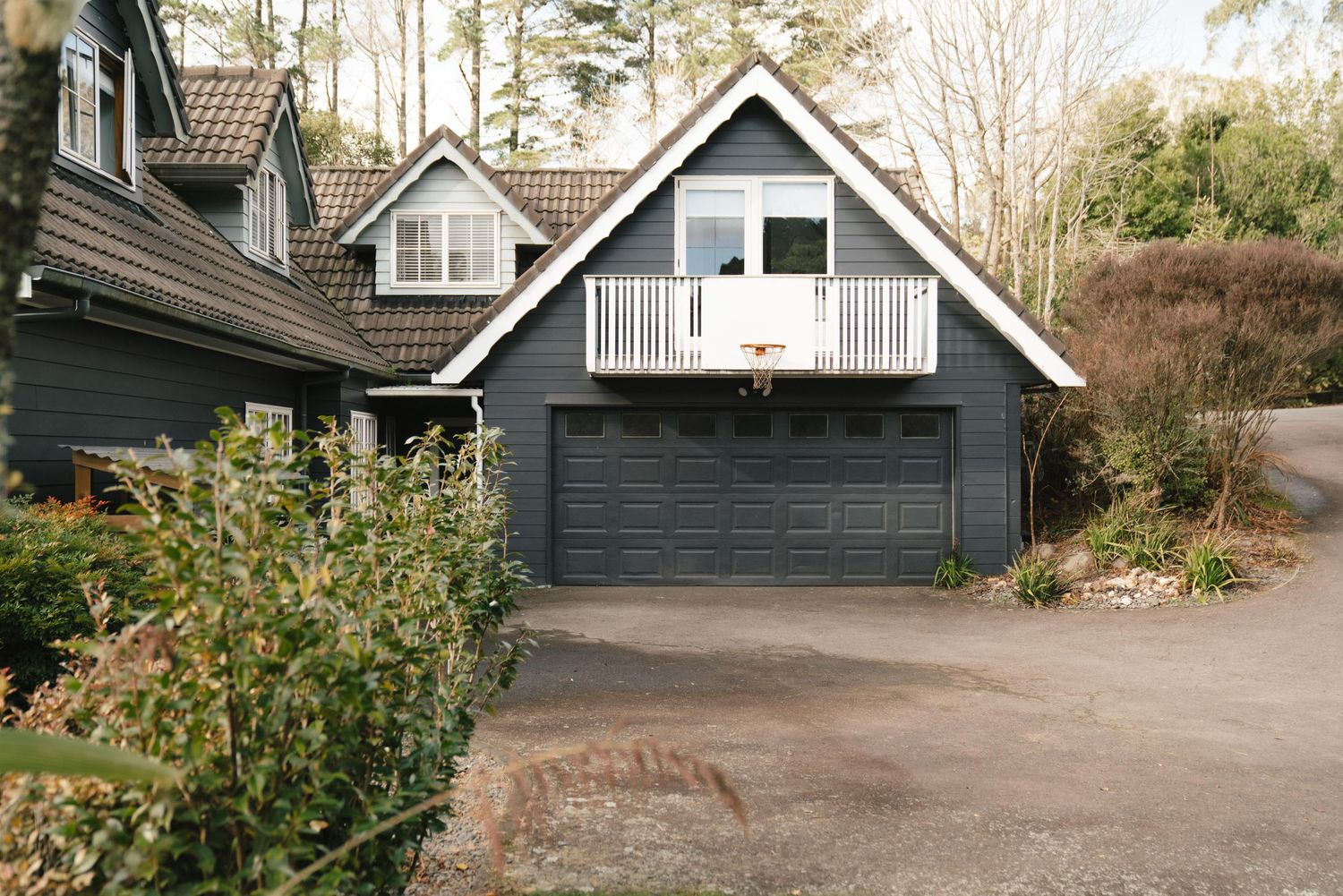 Modern gray house with white-trimmed balcony and attached garage nestled among trees in a wooded setting.