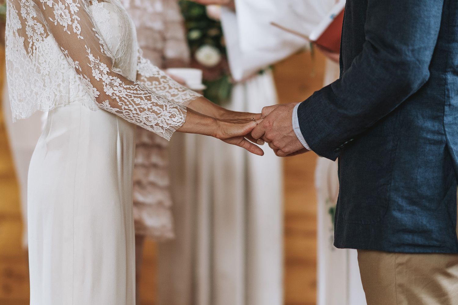 Close-up of hands holding during an intimate wedding ceremony with lace sleeve detail and navy suit.