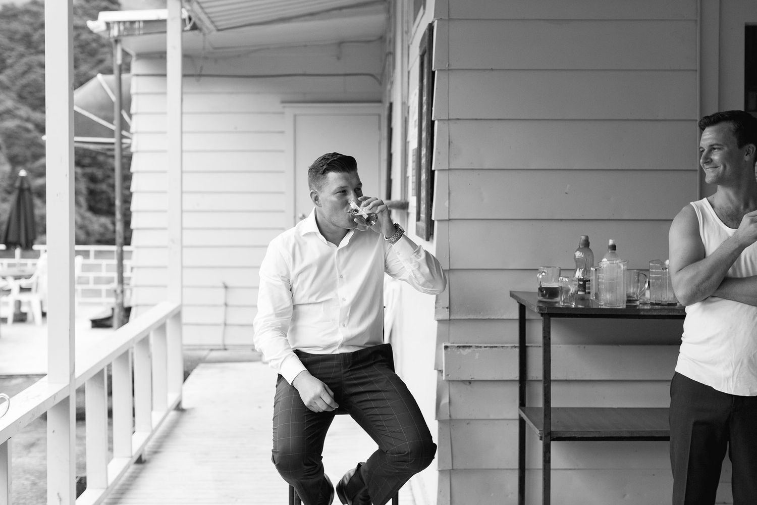 Two people are sitting and chatting on a front porch with white siding in a casual summer scene.