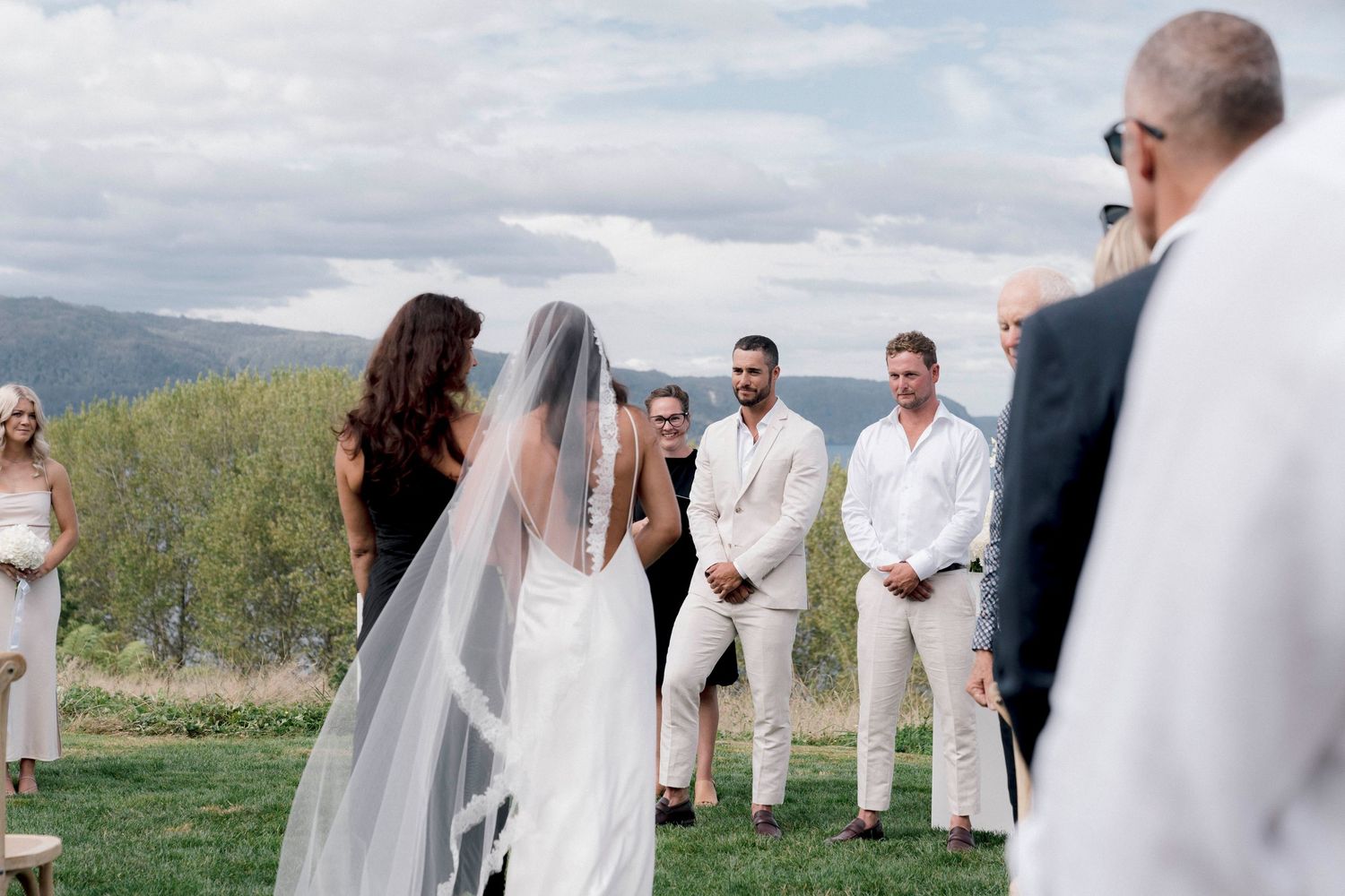 An outdoor wedding ceremony with mountain views and guests in light-colored attire.