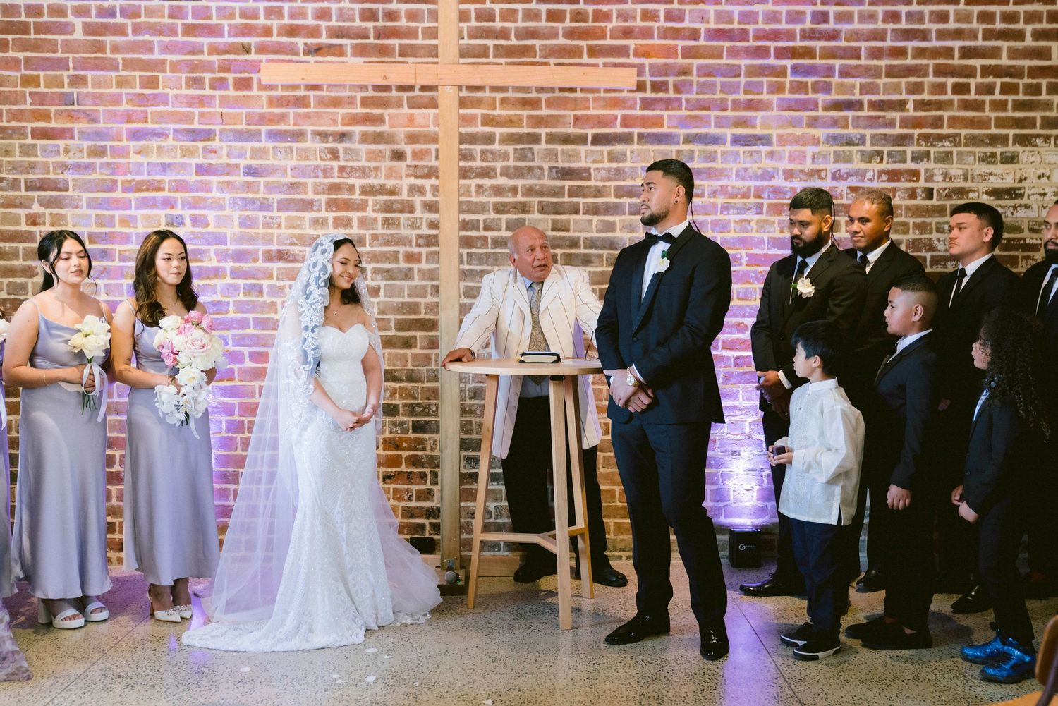 Wedding ceremony in progress inside industrial brick venue with wedding party lined up.
