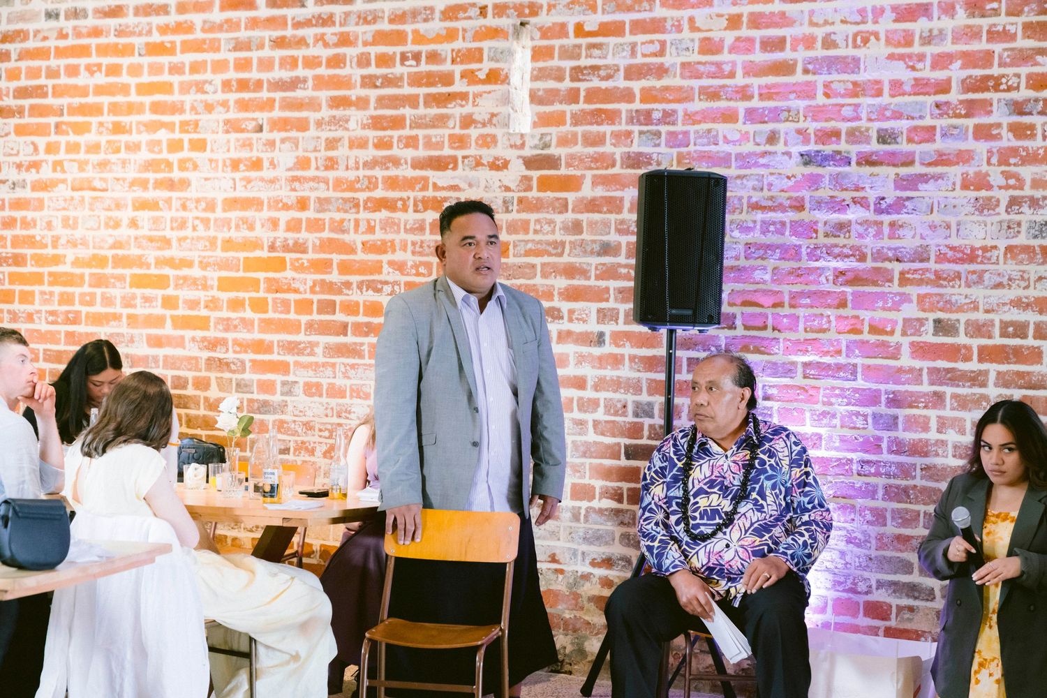 Wedding guests mingle and socialize in a rustic brick venue with purple lighting accents.