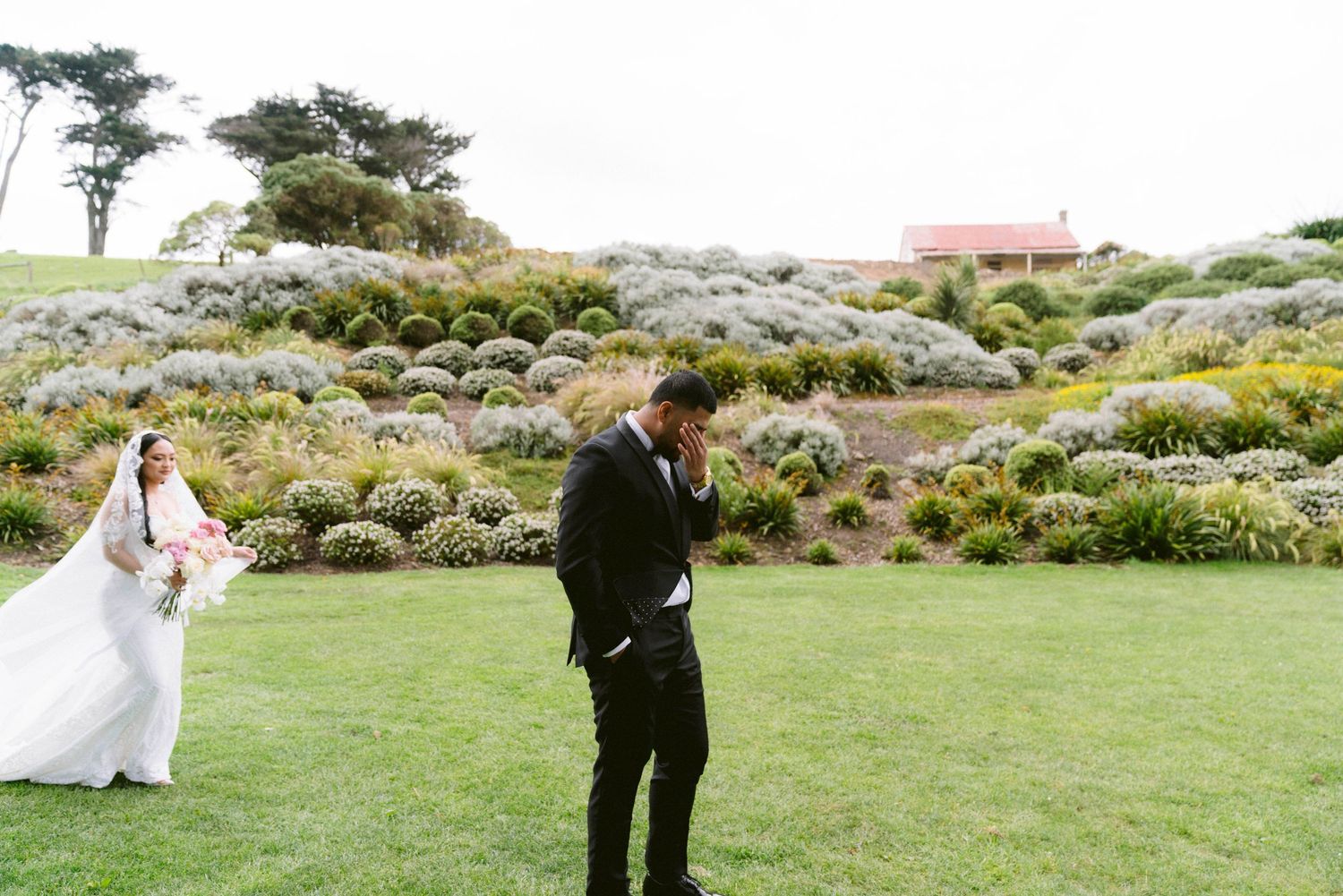 Couple posing for wedding photos in expansive coastal garden with natural rock formations.