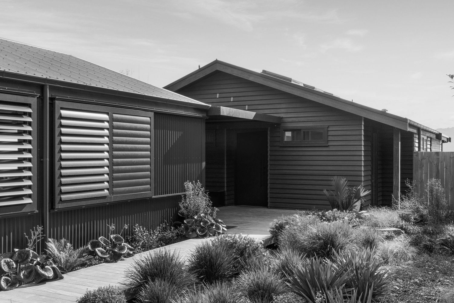 Black and white photo of a modern ranch house exterior with horizontal siding and landscaped garden beds.