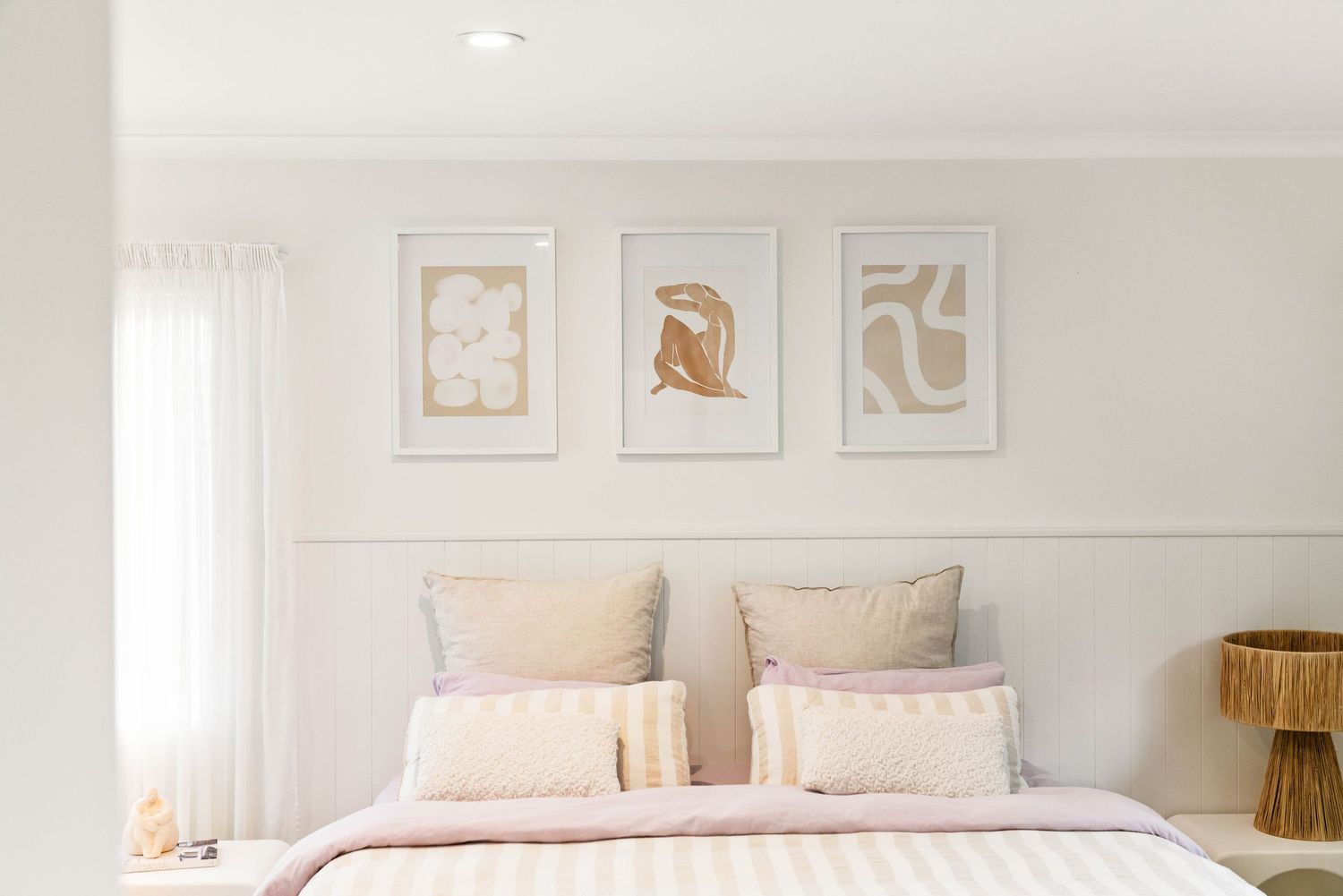 Bright white bedroom interior with neutral decor, framed art prints, and plush bedding creating a serene atmosphere.
