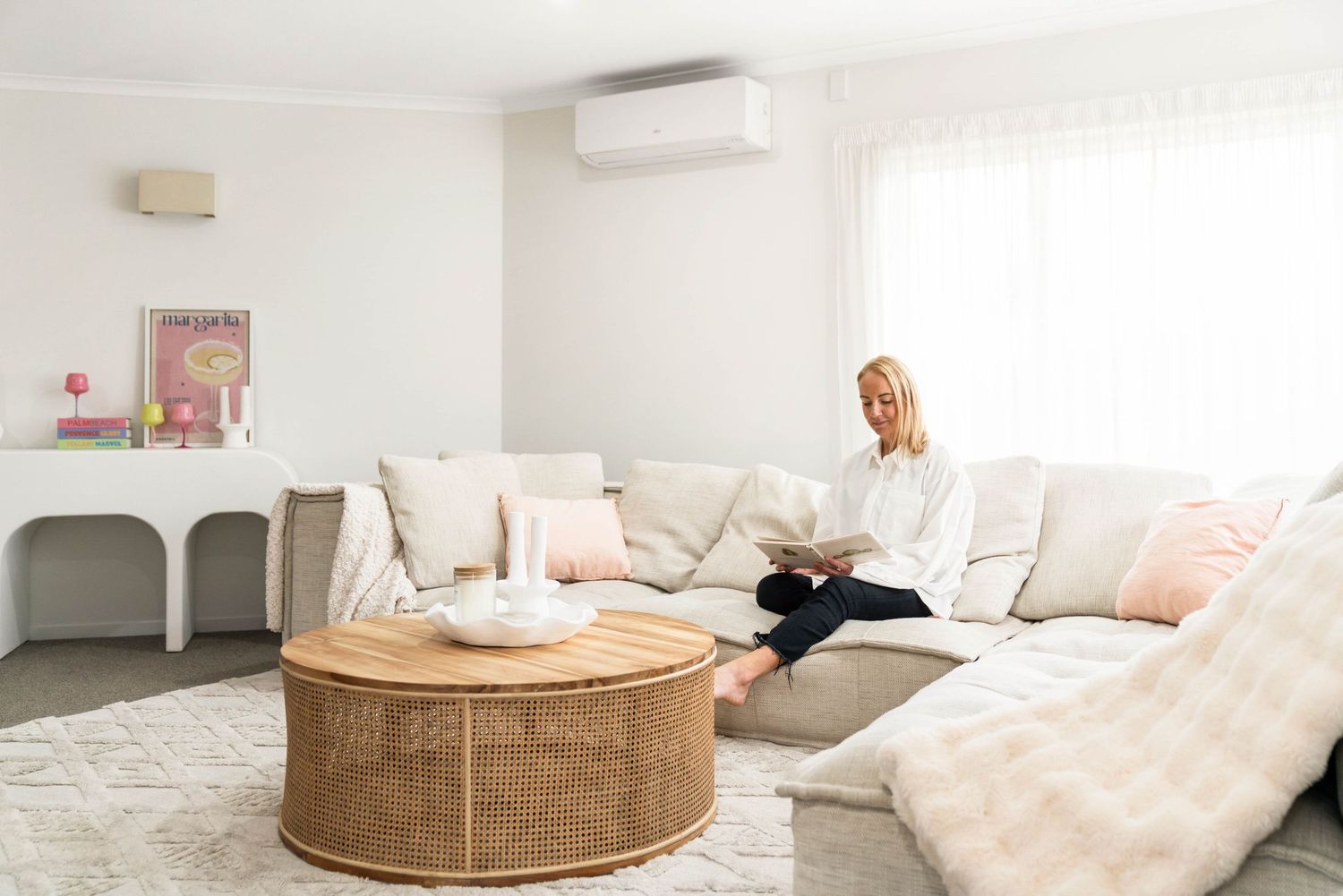 Modern minimalist living room features circular beige ottoman and cozy white cushions against neutral decor.