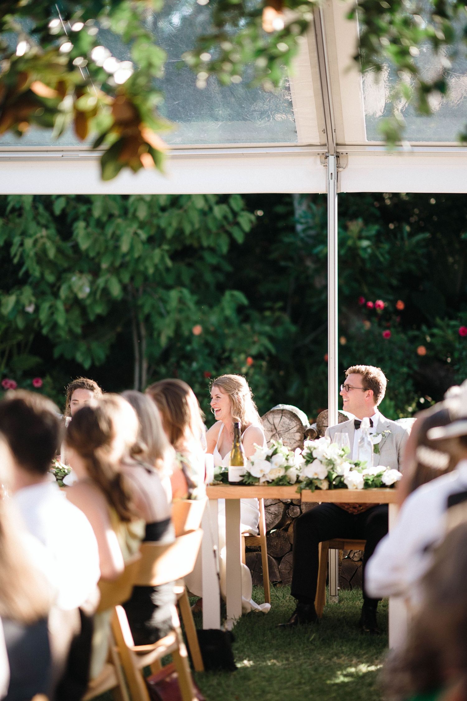 Outdoor wedding reception under trees with long wooden tables and white decor.