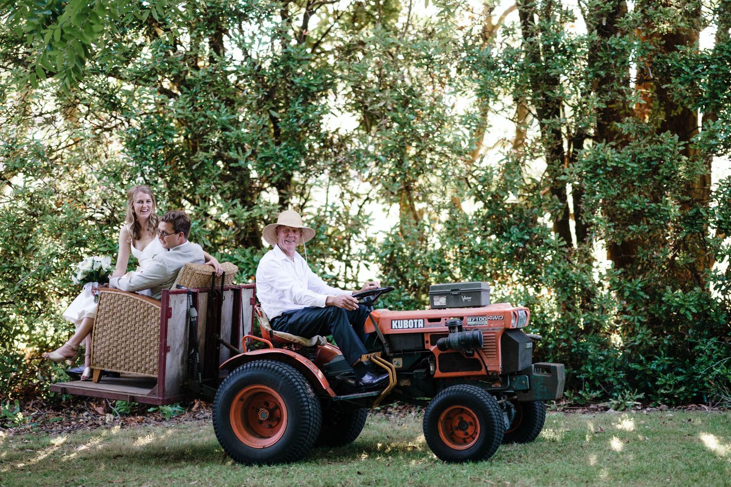 A vintage tractor sits under green trees at a rustic outdoor event.