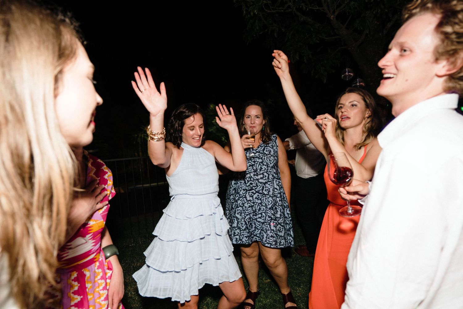 Wedding guests dance and celebrate during outdoor nighttime reception.