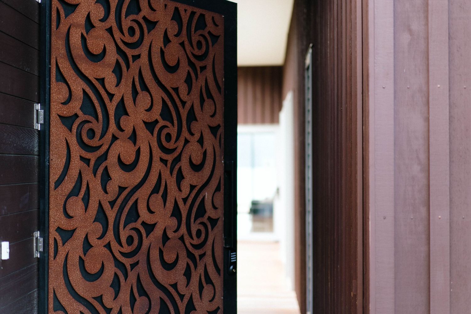 Modern wooden door with ornate brown scroll pattern design against dark frame.