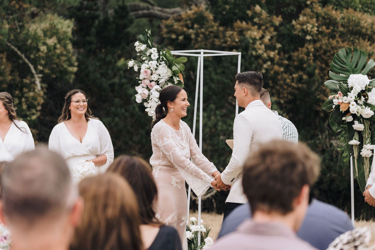 An outdoor wedding ceremony with white floral arrangements and modern geometric arch decor.