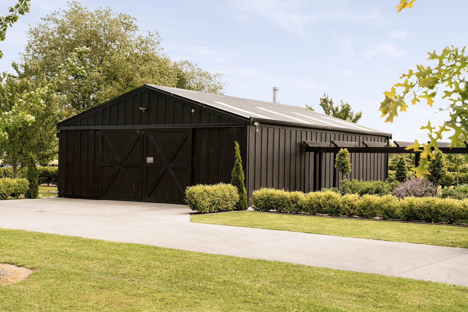 Modern black barn-style building with white trim situated on a manicured lawn with surrounding greenery.