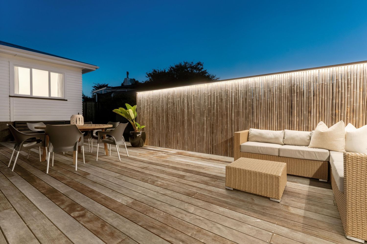 Modern outdoor deck with wicker furniture and wooden wall feature illuminated by LED lighting.