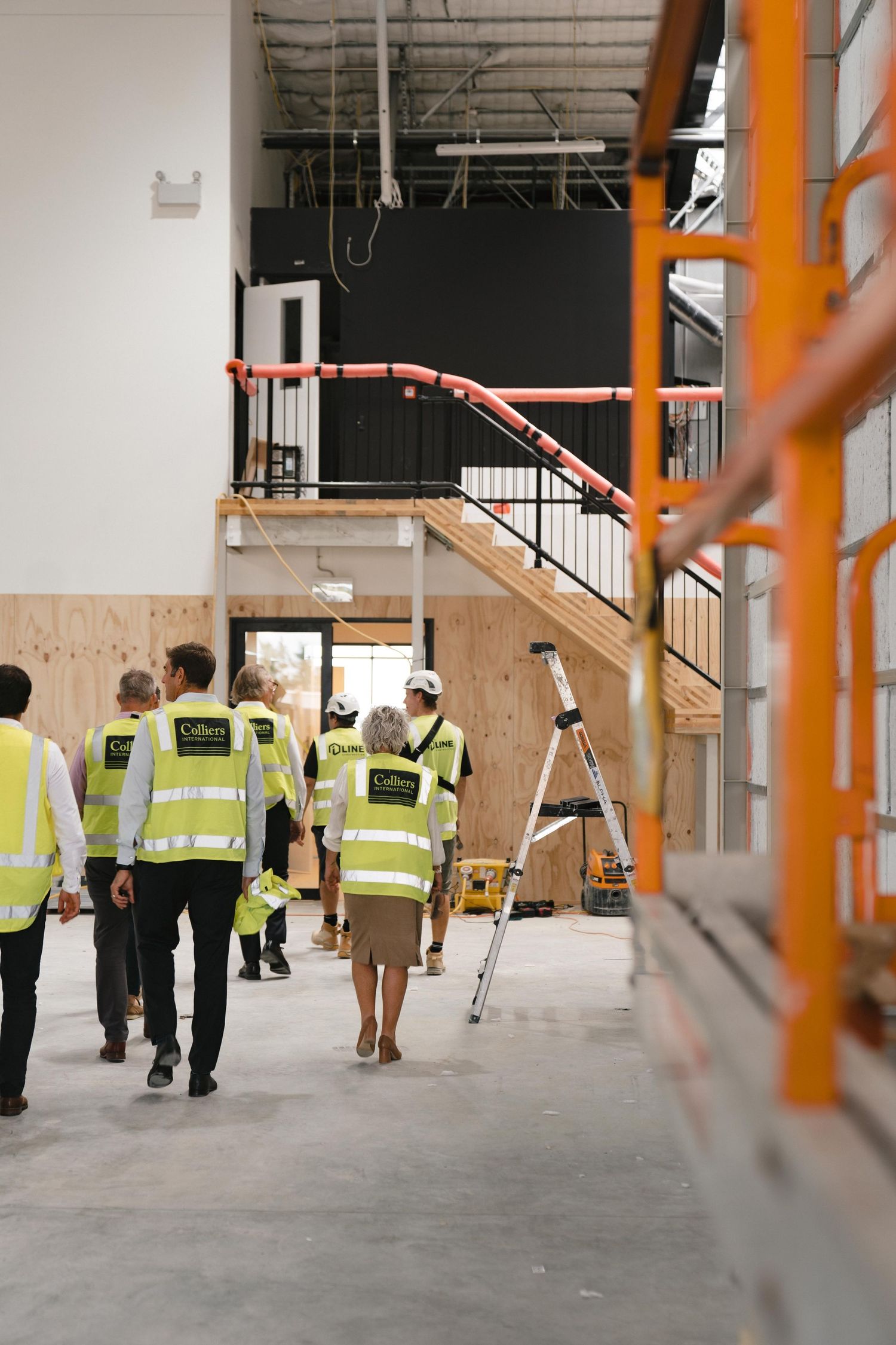 Construction workers in high visibility vests walking through an unfinished commercial building interior.
