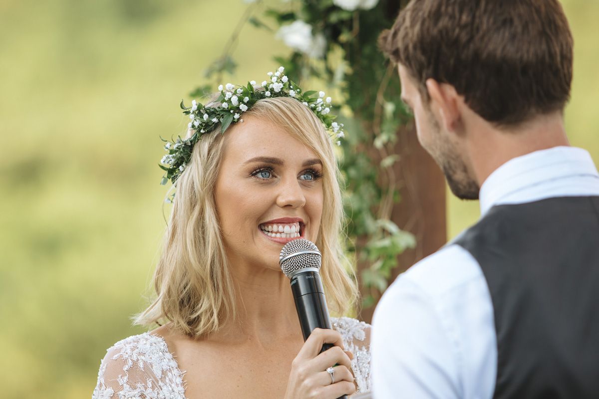 A couple exchanges vows during an outdoor wedding ceremony with the bride holding a microphone.