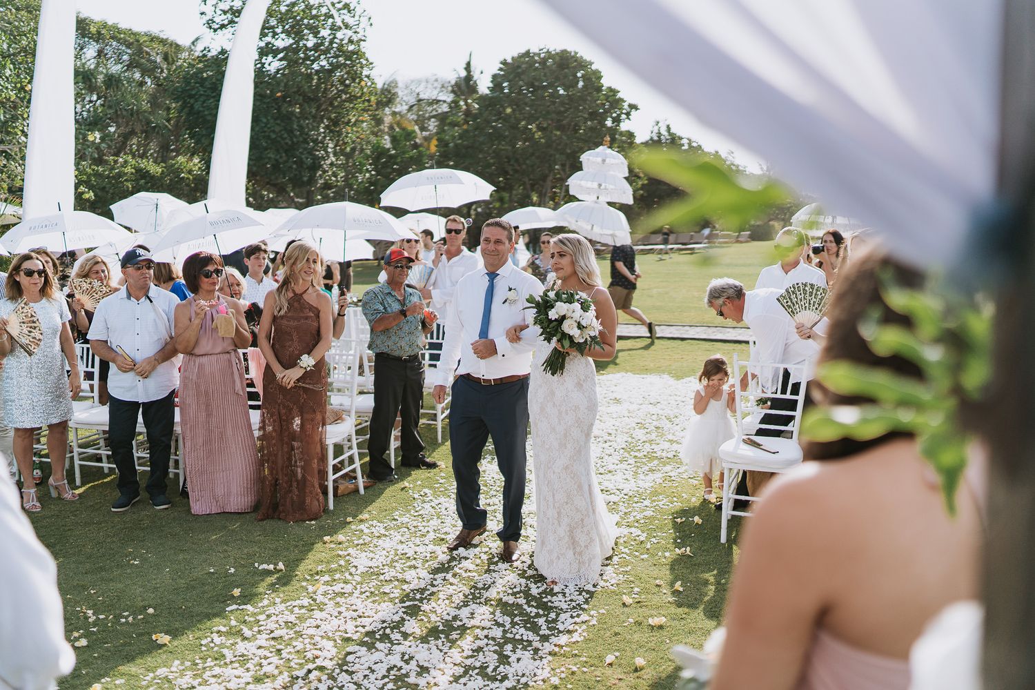 Outdoor wedding reception tables set underneath white tents with green trees in background.