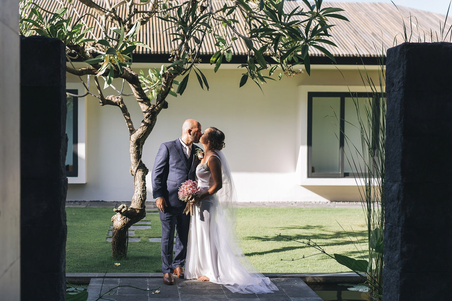 Romantic wedding couple sharing an intimate moment under a tree in a garden setting.