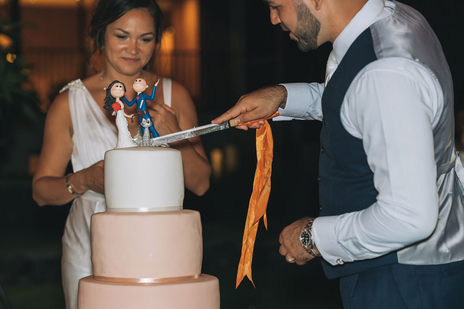 A bride and groom cut into their three-tiered wedding cake decorated with figurine toppers.