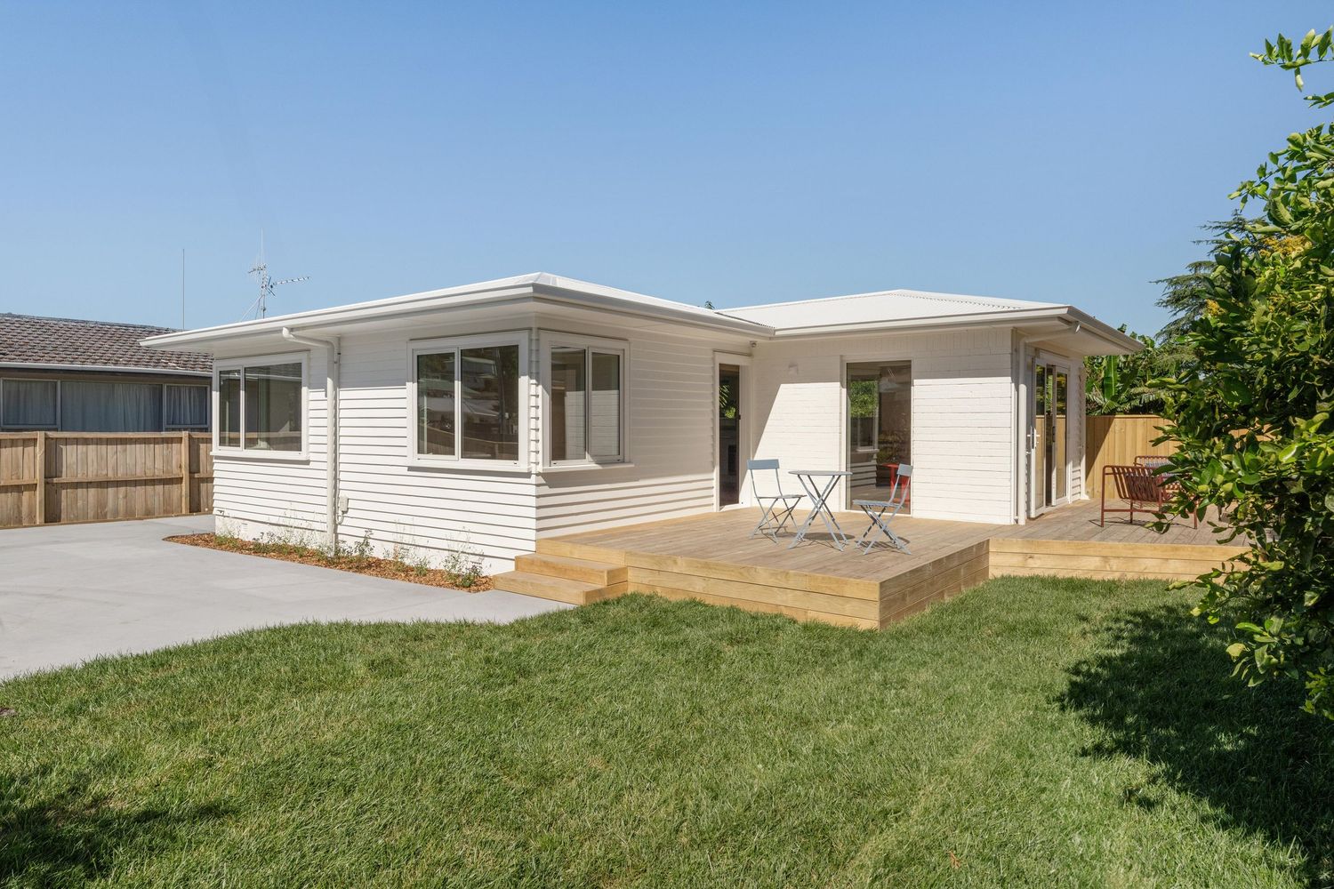 Modern single-story white ranch house with attached carport and wooden deck in a sunny backyard setting.