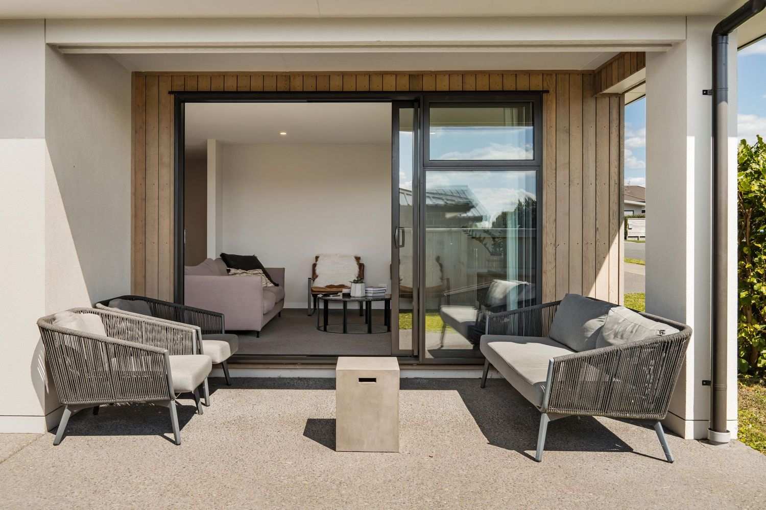 Modern patio space with gray outdoor furniture and concrete accent table on an aggregate stone surface.