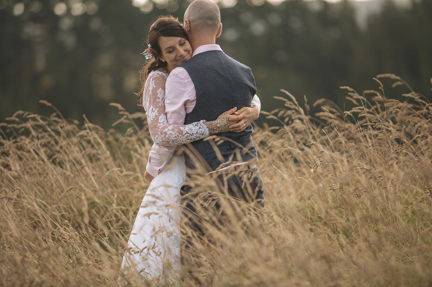 A romantic couple embraces in a sunlit meadow of tall golden grass during golden hour.