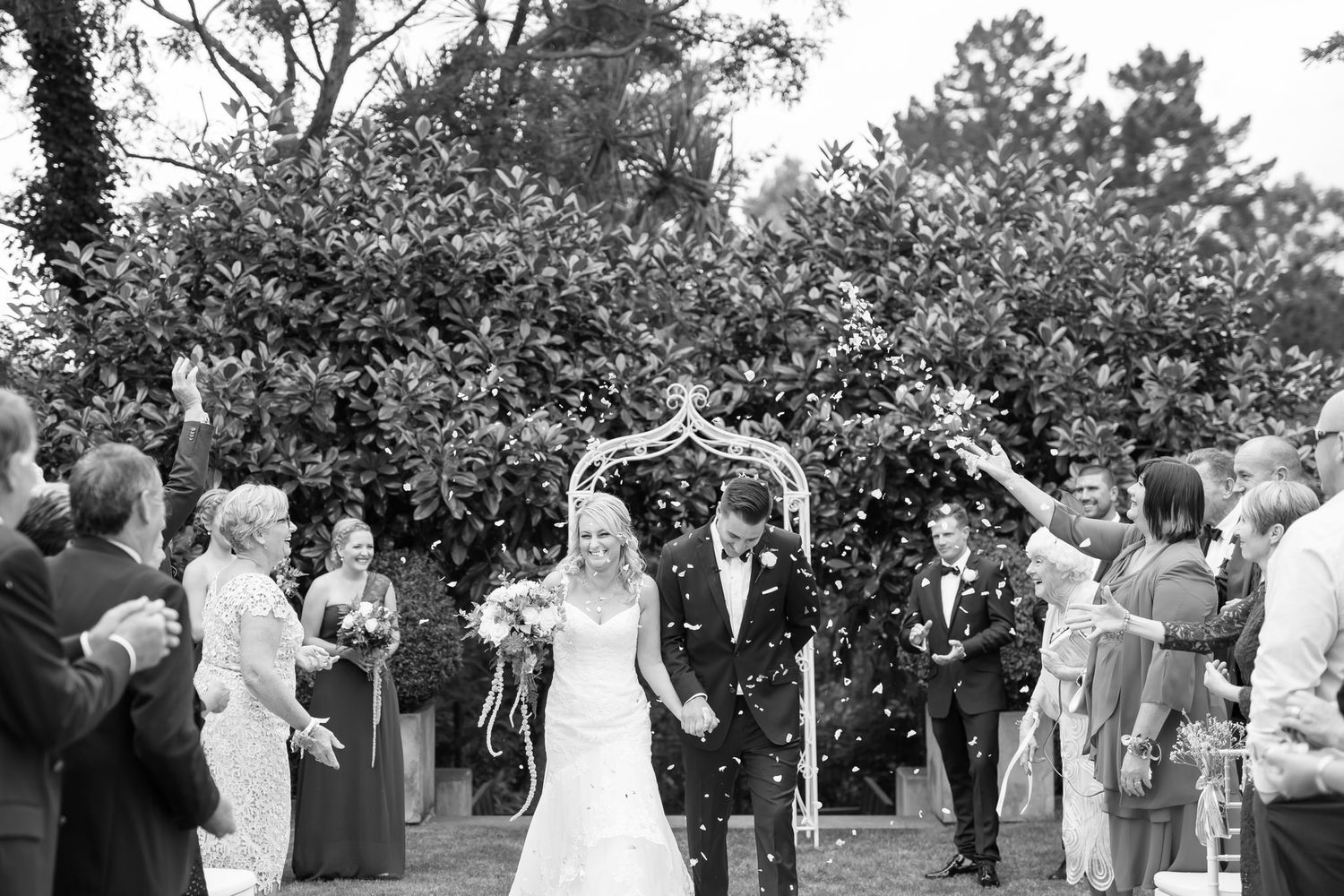 A joyful celebration with bubbles being blown at an outdoor garden wedding ceremony.
