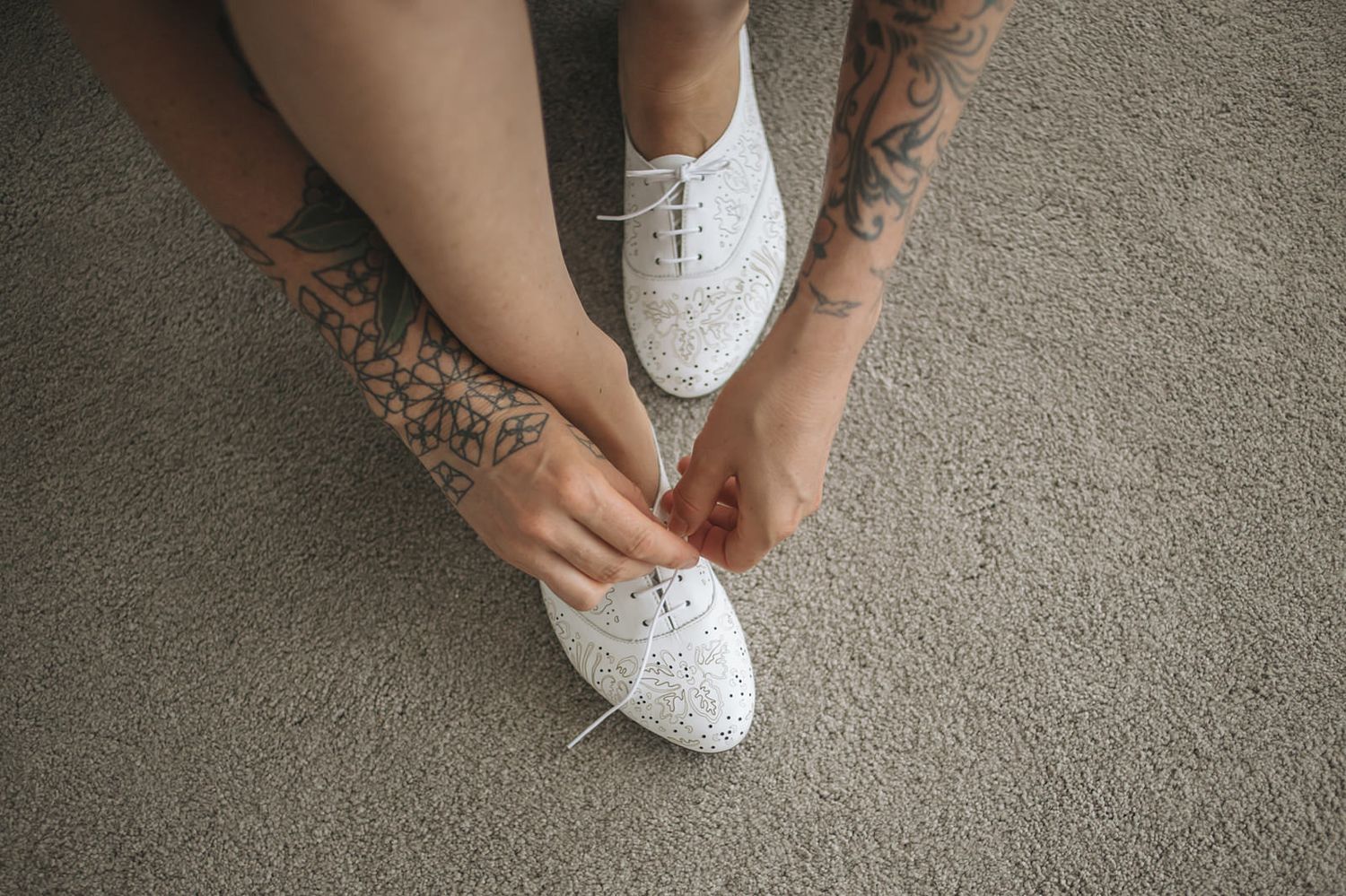 Close-up view of glittery white bridal shoes being put on before a wedding ceremony on grey carpet.