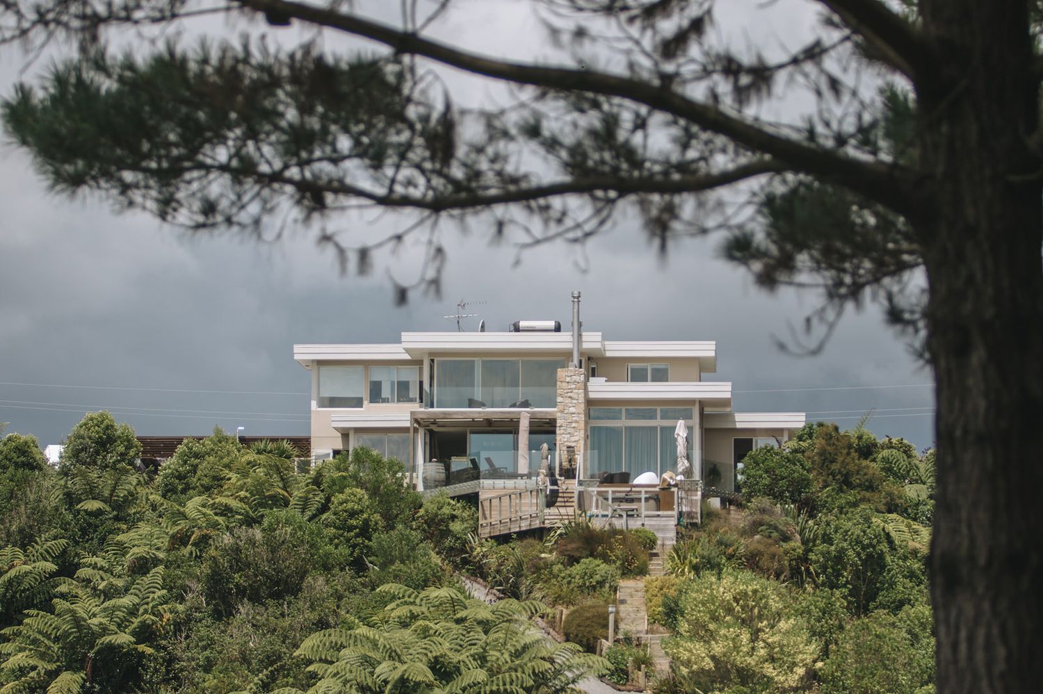 Modern luxury villa with angular architecture perched on a hilltop overlooking dense green forest canopy under cloudy skies.