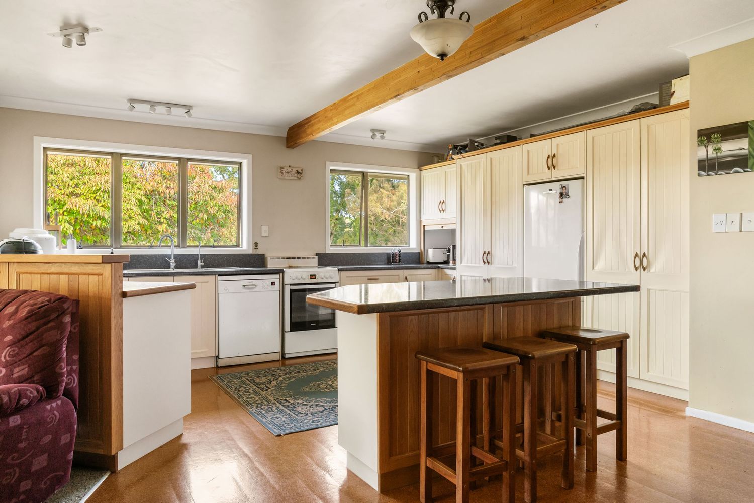 Modern kitchen with wooden floors, white cabinets and breakfast bar featuring exposed ceiling beams.
