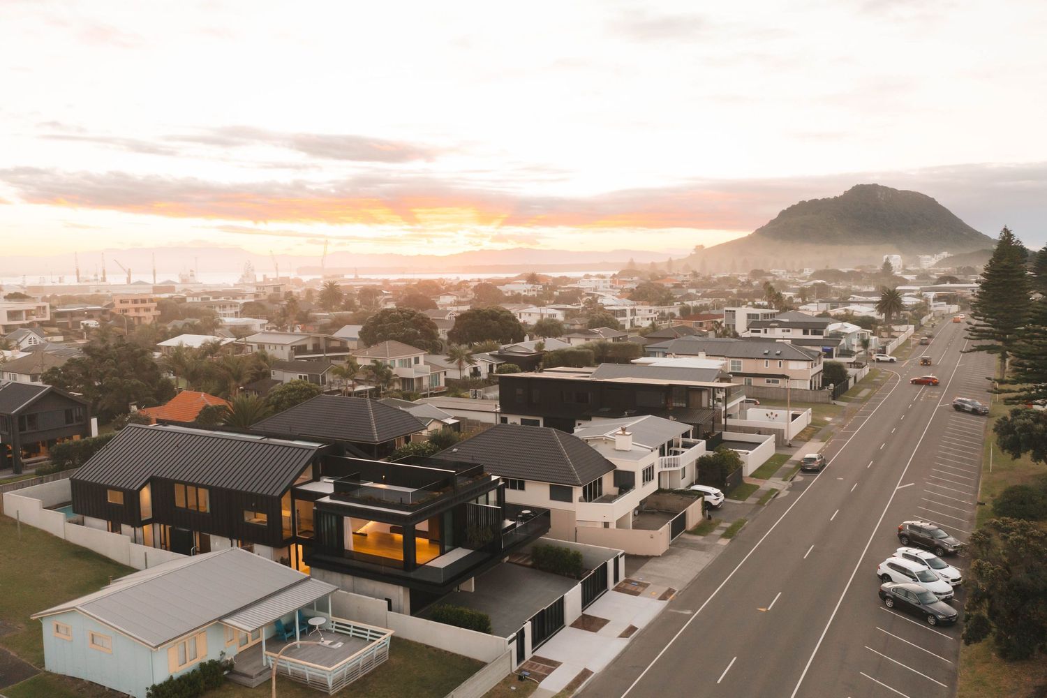 Panoramic aerial view of coastal suburban neighborhood at sunset with mountain backdrop.