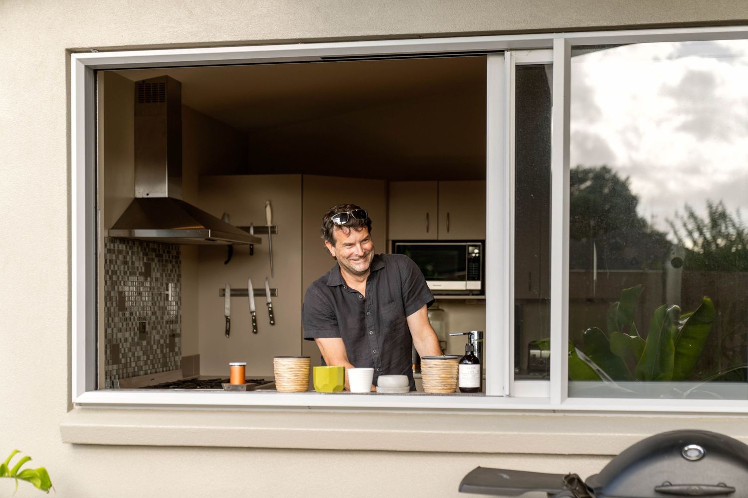 View through a kitchen window showing coffee and drink containers arranged on a counter with a dark hood vent visible above.