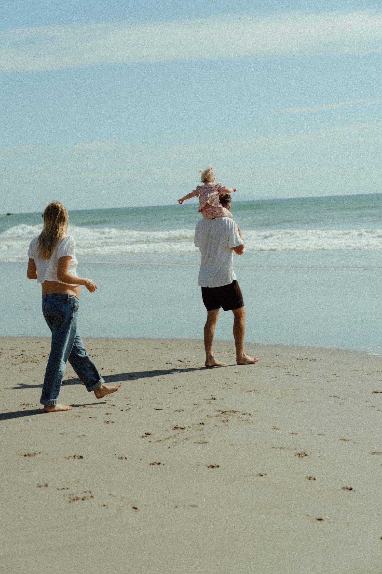 A family enjoys a sunny day together walking and playing on a sandy beach with ocean waves in the background.