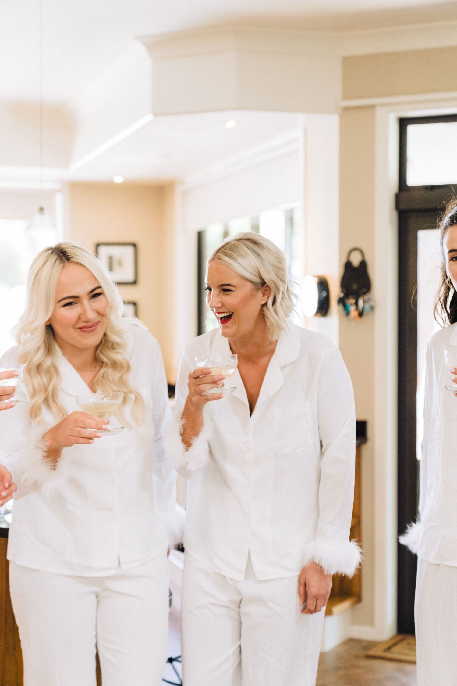 Three people wearing matching white robes smile and laugh together while holding drinks during a celebration.